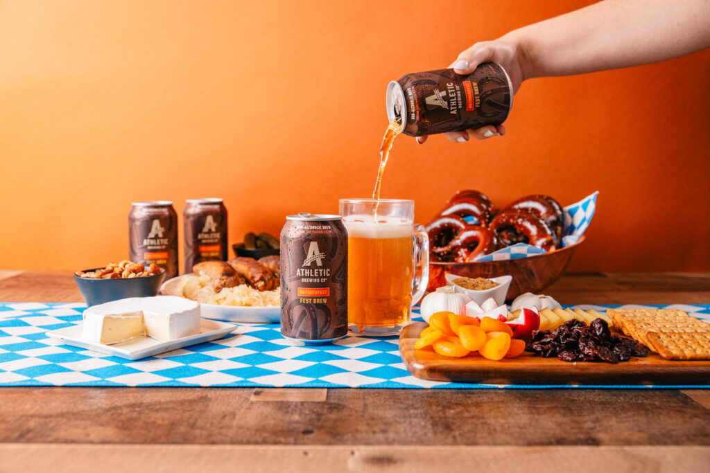 Athletic Brewing's non-alcoholic Oktoberfest beer being poured into a glass alongside pretzels and german food
