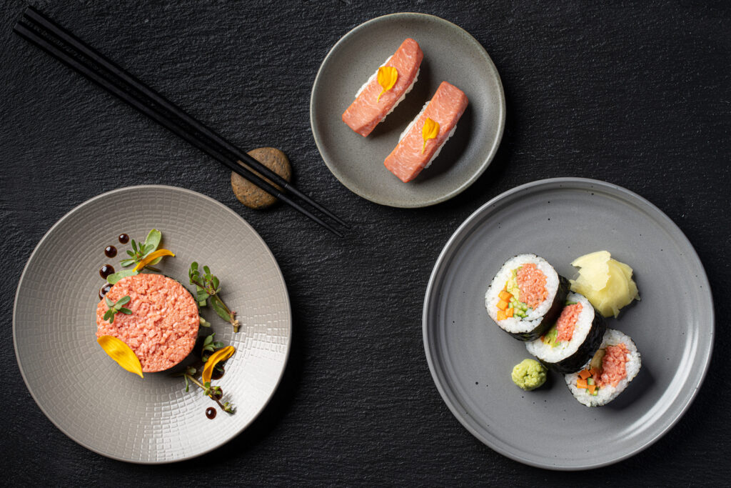 Three labgrown Blue Nalu seafood meat plates including a salmon burger, nigiri, and sushi rolls