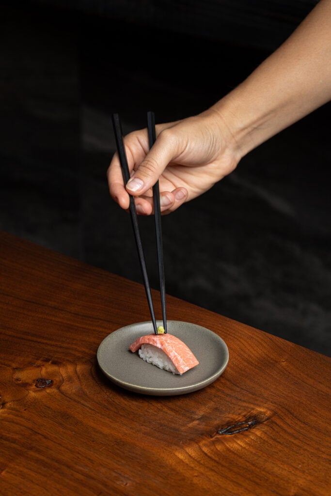 Person picking up labgrown seafood meat sashimi with chopsticks