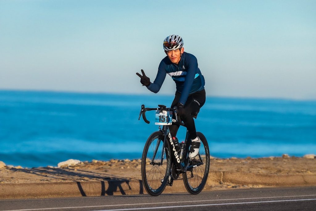 Cyclist on the road along the Pacific Ocean giving the peace symbol