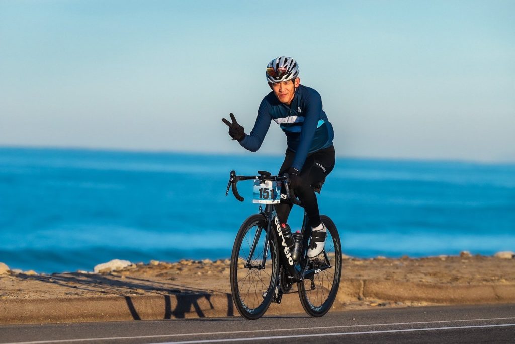 Cyclists riding along the road along the Pacific Ocean giving a symbol of peace