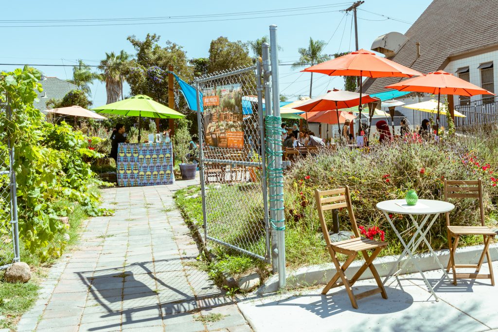 Exterior of MAKE Projects & Cafe in San Diego featuring a table, umbrellas, and their community garden