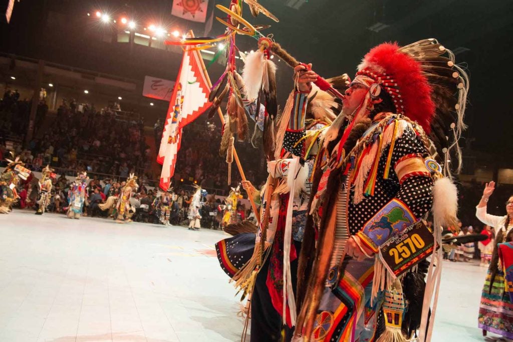 Native American in traditional outfit playing a horn at the Gathering of Nations event  