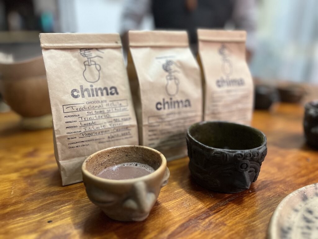 Oaxacan hot chocolate in decorative mugs in front of bags titled Chima