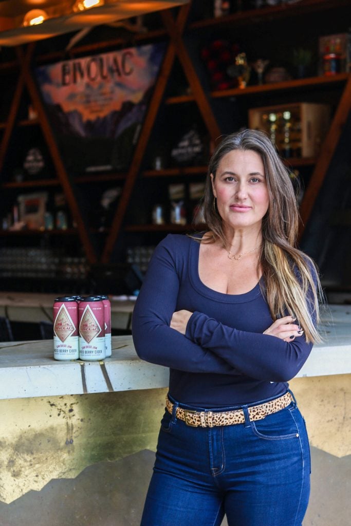 Bivouac Ciderworks co-founder Laura Worm standing infront of six pack of cider