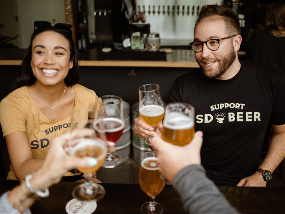 SD Food News: The 2023 San Diego Beer Week commences and beer enthusiasts toast in front of a bar