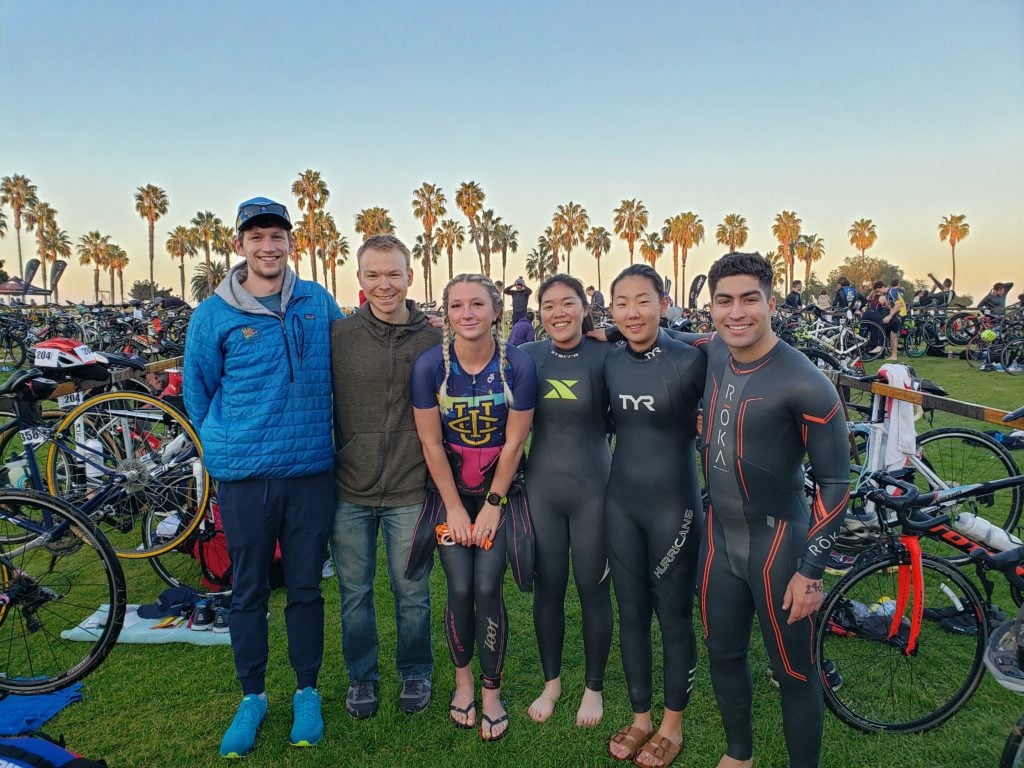 Tritonman Triathlon in San Diego featuring competitors huddled in wetsuits with bikes behind them