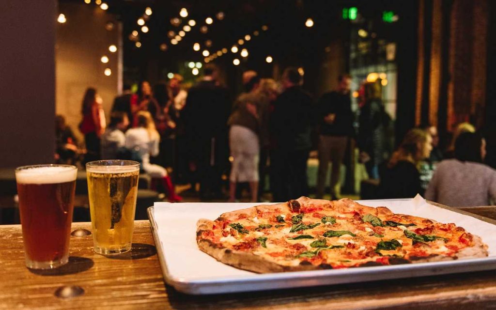 Interior of Basic Bar & Pizza featuring a table with large groups a margarita pizza and two beers