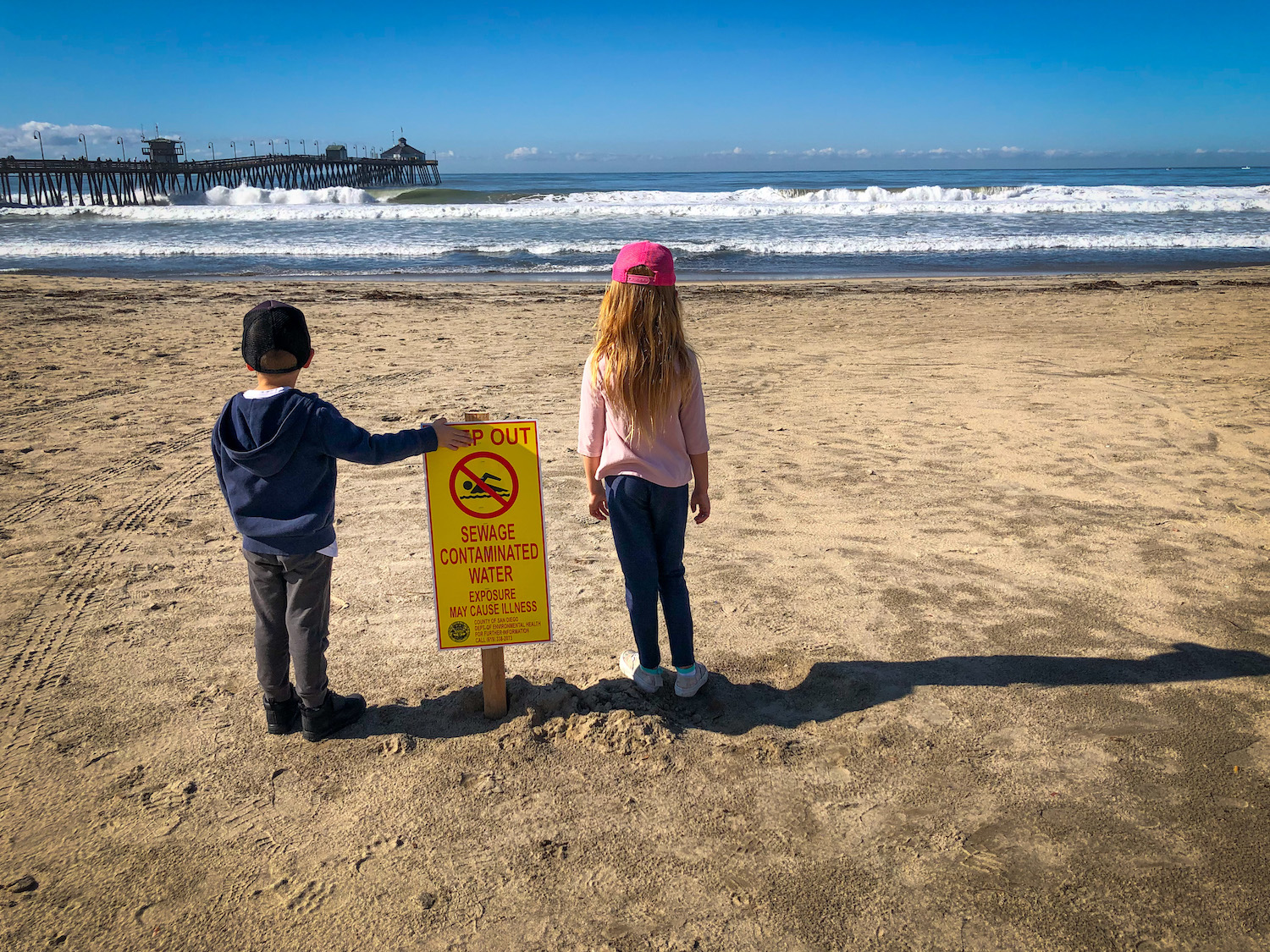 Two little kids standing by a beach contamination sign at Imperial Beach