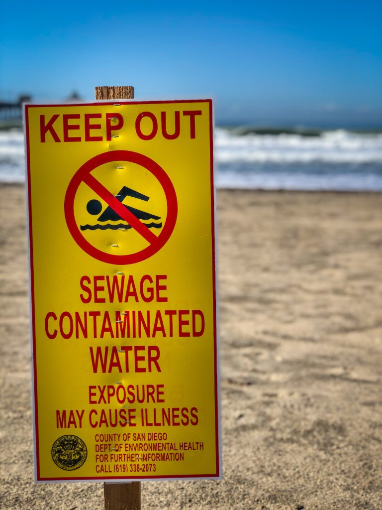 Yellow sign reading "Keep out. Sewage contaminated water. Exposure may cause illness" at imperial beach, San Diego