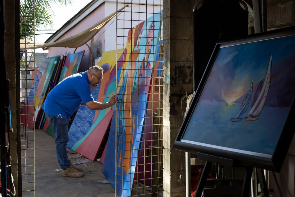 Mexican artist Enrique Chiu painting in his studio outside featuring a sailboat panting in the foreground