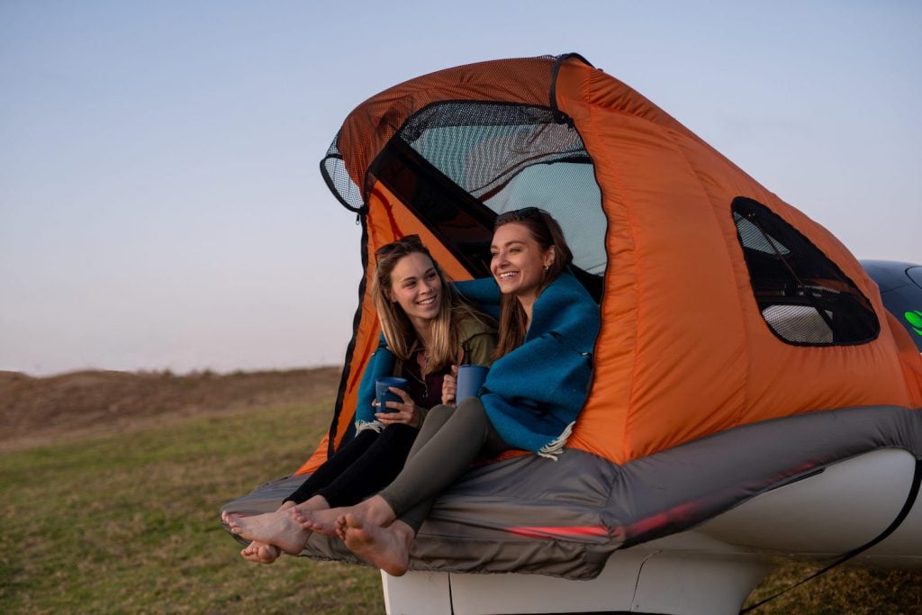 Aptera electric vehicle with trunk open and featuring convertible shelter featuring two women who are camping 