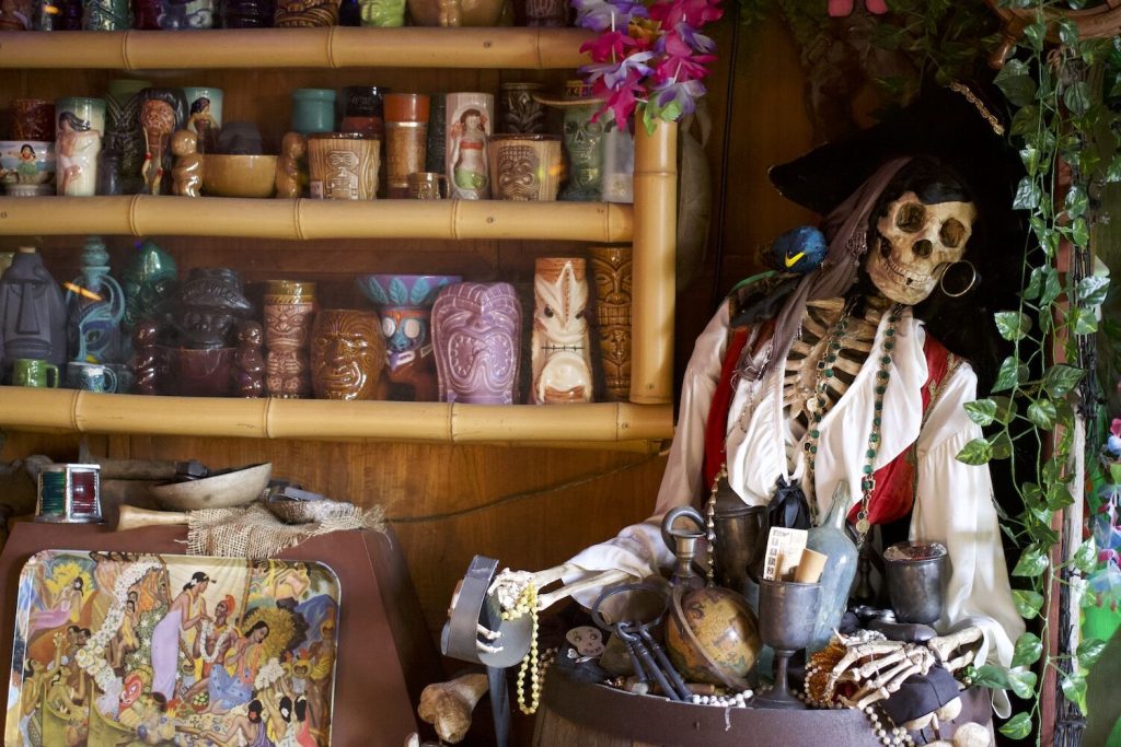 Skeleton dressed in pirate attire surrounded by booty, tiki glasses, and other island collectables found in the backyards of San Diegans