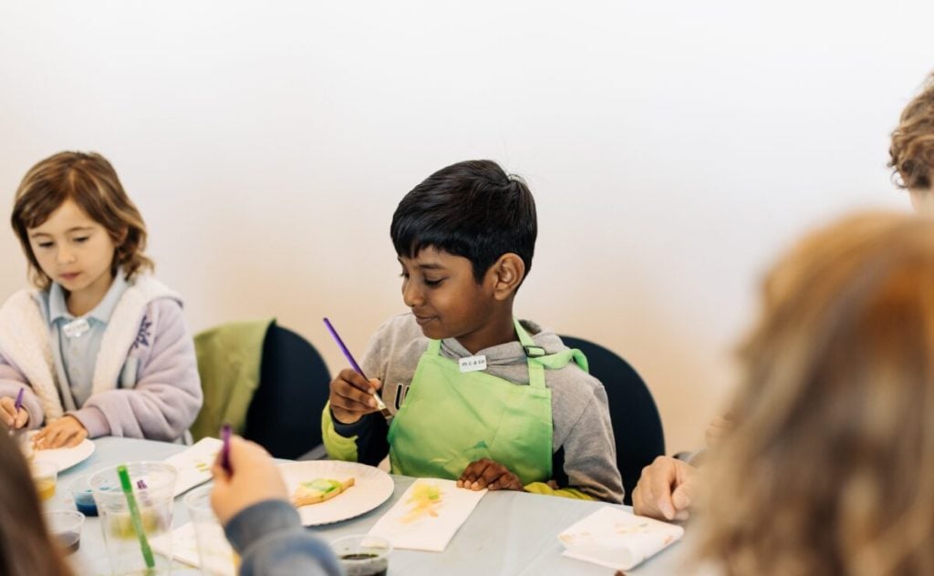 Kids working on an art piece and holding a paint brush at the Museum of Contemporary Arts San Diego