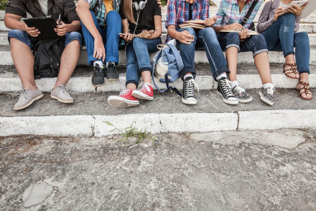 The feet of teens and young adults while sitting on steps reading, using their phone, and conversing with each other