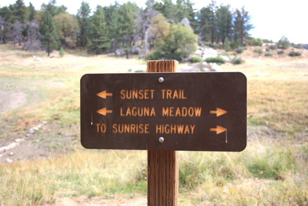 A trail sign from Mt. Laguna in San Diego with the words "Sunset Trail", "Laguna Meadow", and "To Sunrise Highway" with arrows pointing in different directions 
