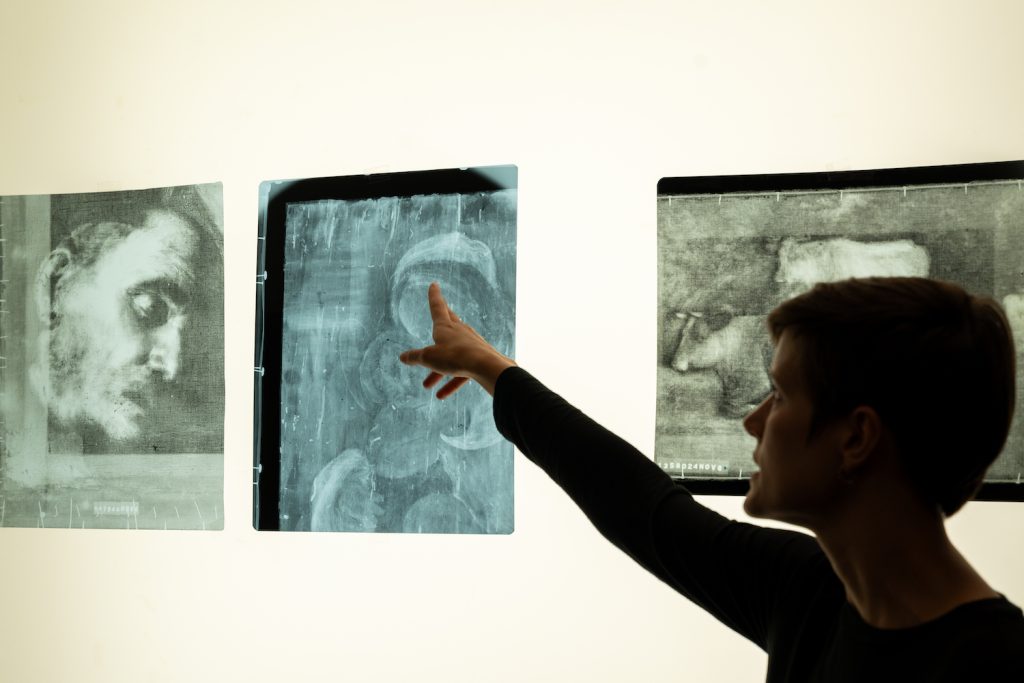 A Balboa Park art conservator stands in front of a projection of X-ray scans showing how historic painting often have hidden details beneath layers