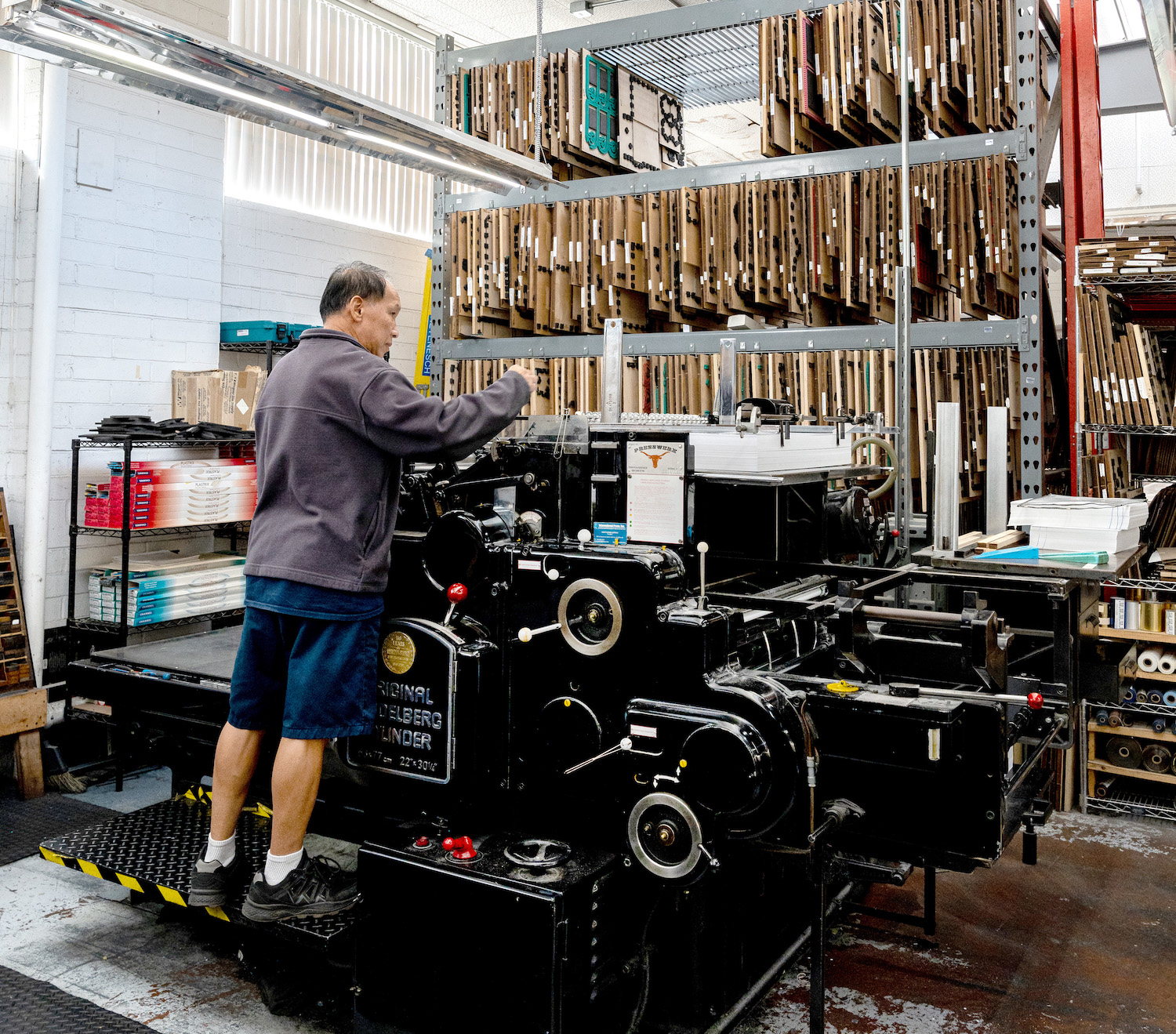 An employee of Neyenesch Printers operating the Original Heidelberg Cylinder printing press built in 1960