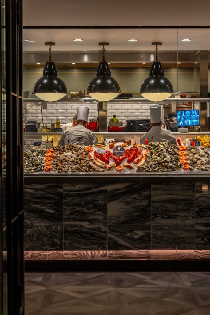 The raw bar at Del Mar's Steak 48 steakhouse featuring lobster, oysters, prawns, and more on ice in front of the kitchen
