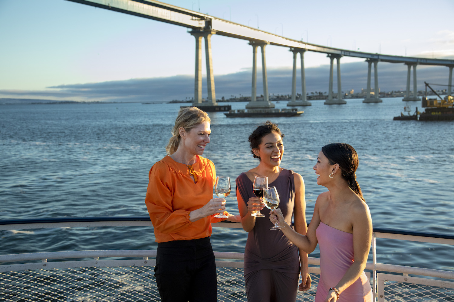 Three women on the deck of a ship in San Diego Bay enjoying a glass of wine aboard City Experience's January brunch cruises