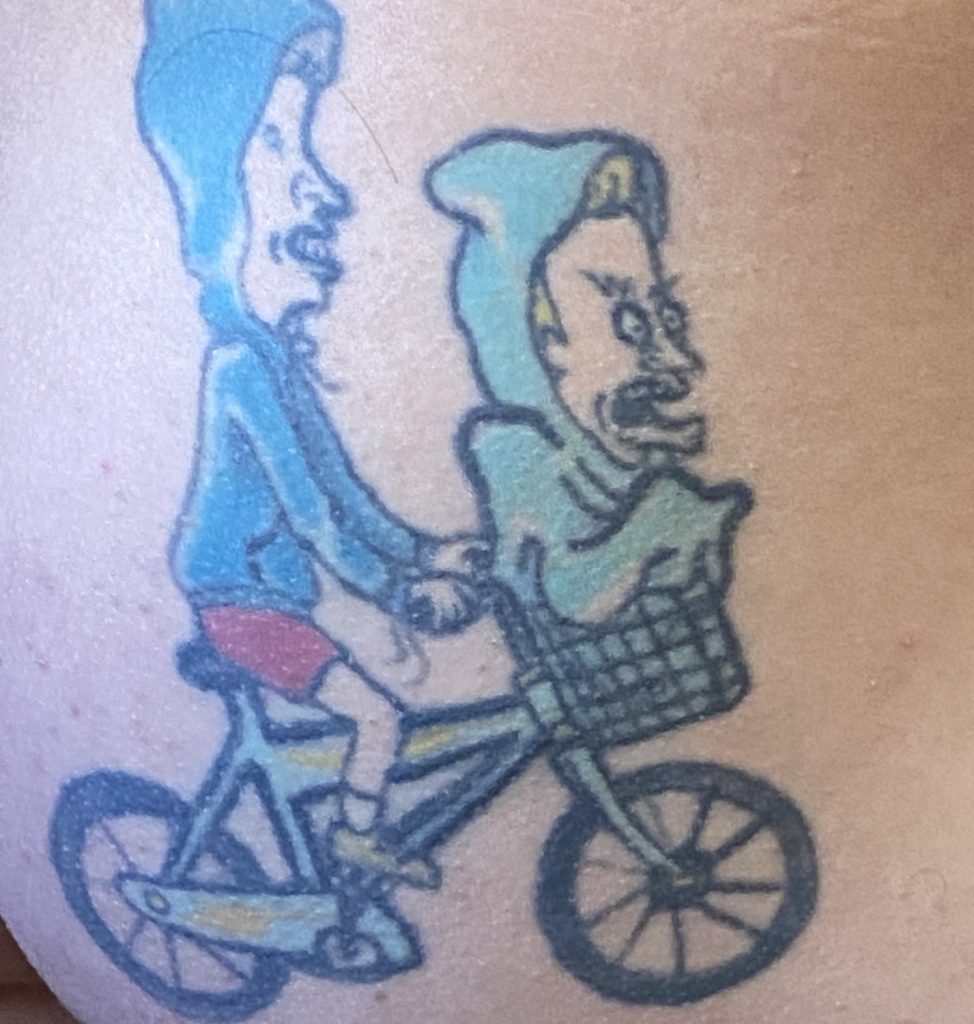 A man's buttcheeks with a tattoo of Beavis and Butt-Head riding a bike emulating the iconic scene in the movie E.T.