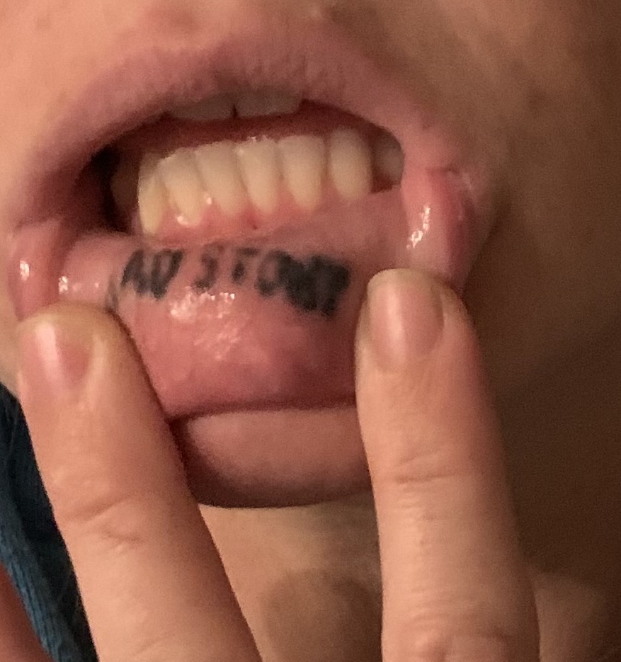 San Diego Magazine's user submitted regrettable tattoos featuring a lip tattoo with the text "Sad Story" in poor handwriting 