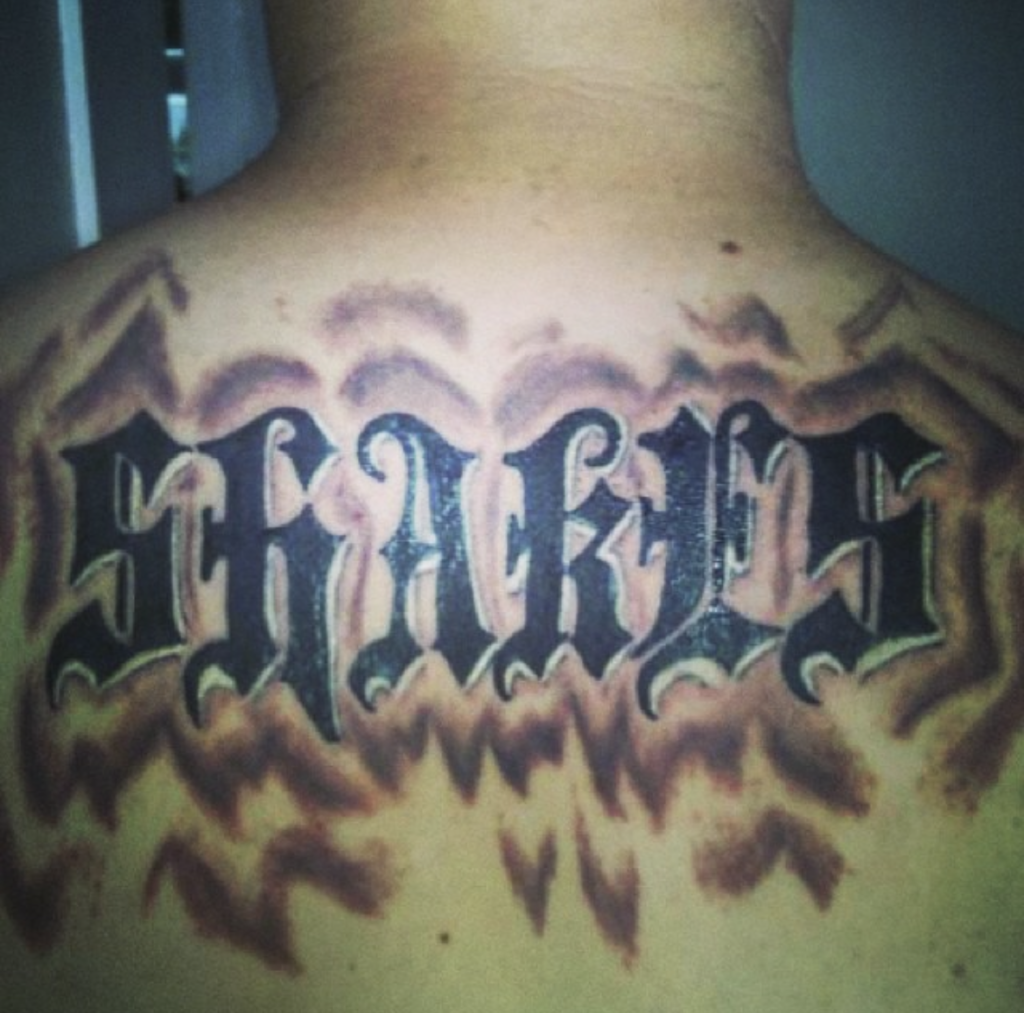 A man's shoulders tattoo with the word "Shakes" in a very obnoxious font