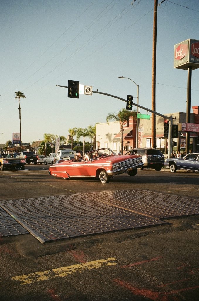 Film photo of a red vintage lowrider car driving down the street in National City by 619 Gurlz photographer Delana Delgado