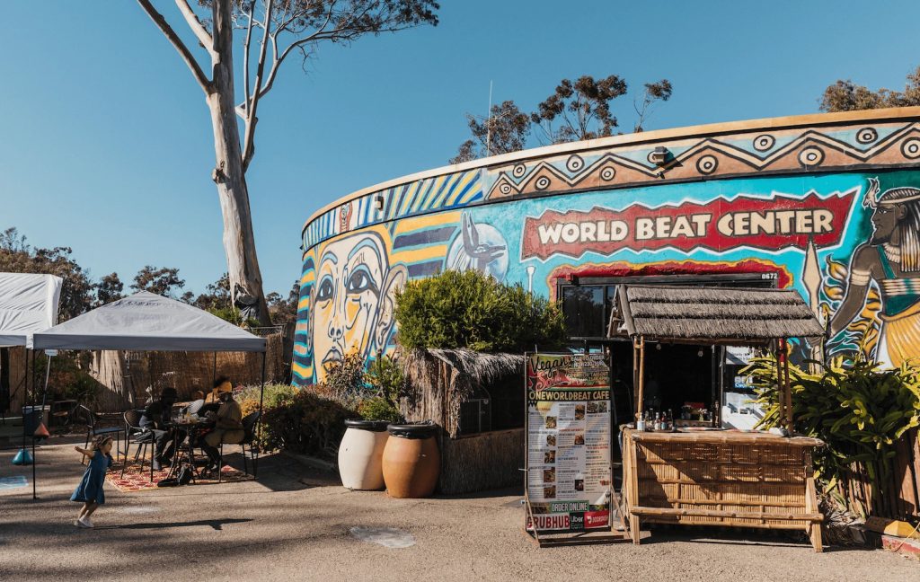 Exterior of the World Beat Center featuring colorful murals and a kid playing out front in Balboa Park, San Diego