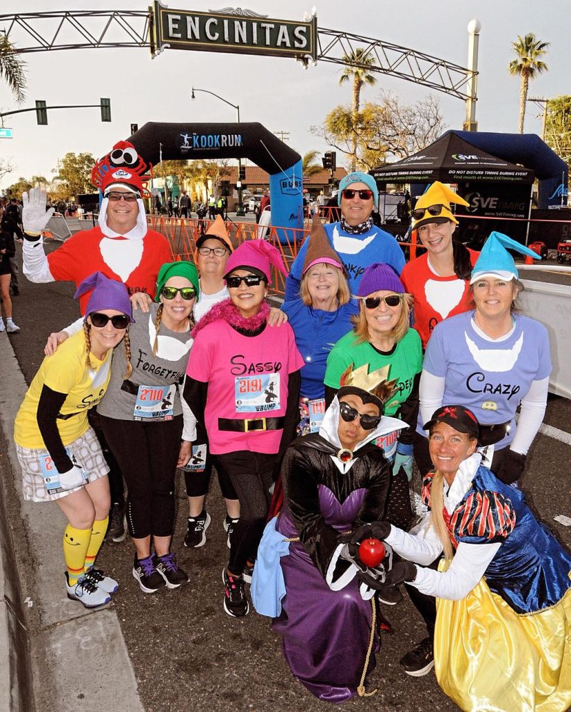 Cardiff Kook Run 2024 featuring runners dressed up as Snow White and the seven dwarves in front of the Encinitas sign in San Diego