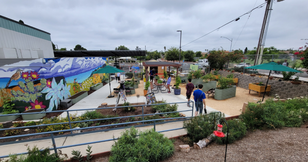 Best new San Diego playgrounds and parks including Park de la Cruz in City Heights featuring a community garden, a colorful mural, and people gathering gardening supplies