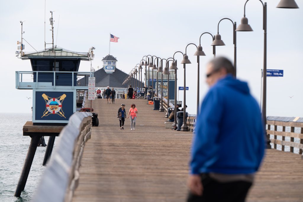 People walking on the Imperial Beach pier located in the South Bay with the lifeguard tower and pier restaurant in the background