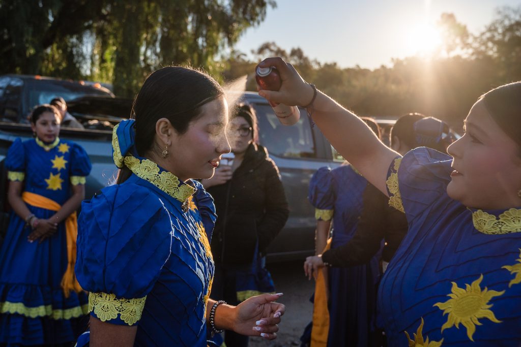San Diego Escaramuza team Las Reynas del Sol’s applying sunscreen to each other while wearing blue and yellow traditional dresses 