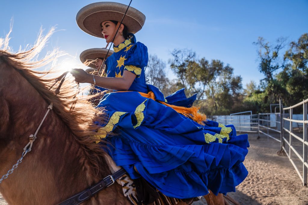 Member of San Diego Escaramuza team Las Reynas del Sol’s riding a horse and wearing a dress made by a seamstress in Mexico