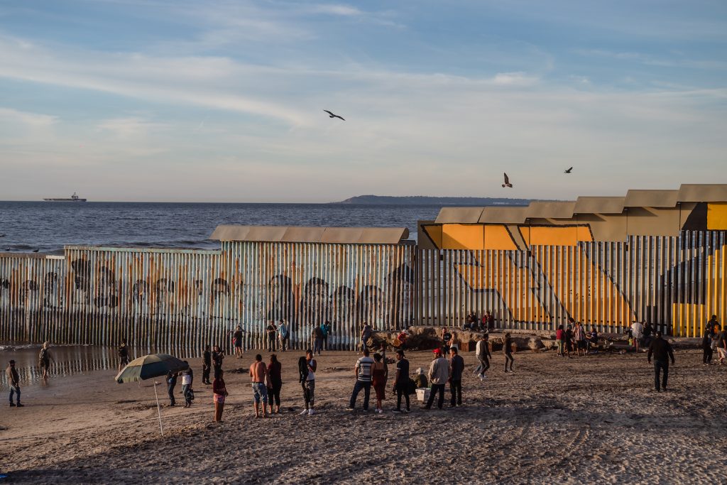 Tijuana residents at the beach in Tijuana looking at  murals on the Tijuana-San Diego border wall with the San Diego coastline in the background