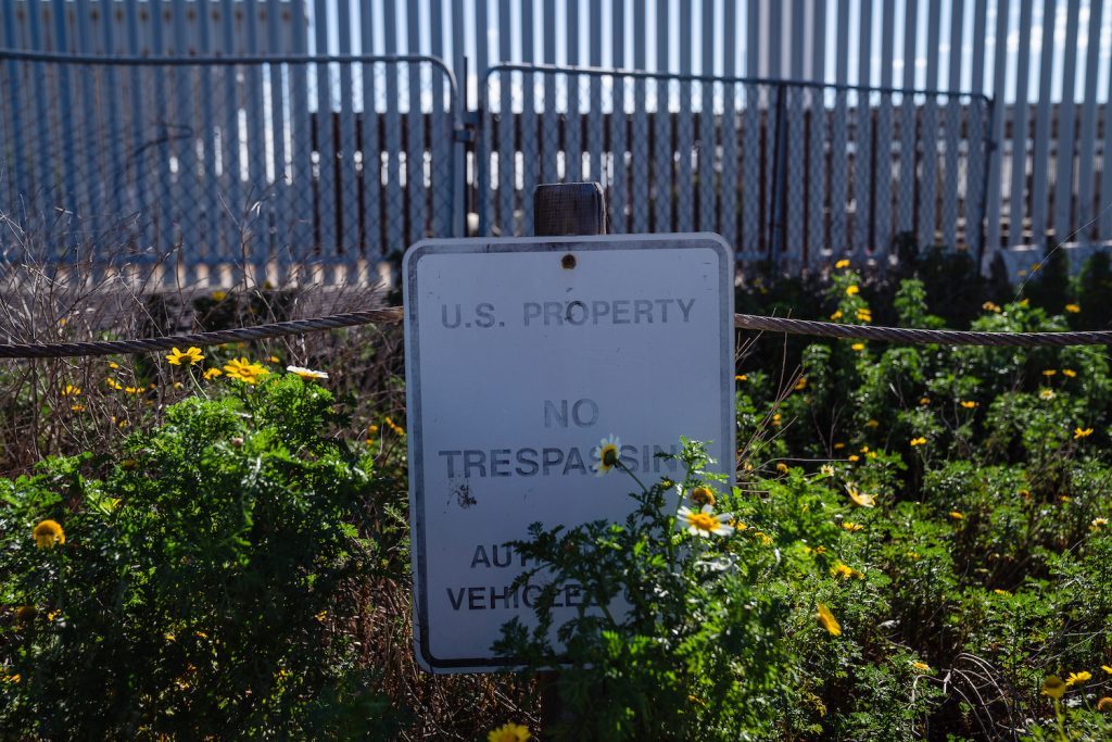 A "No Trespassing" sign hidden behind plants and flowers at Friendship Park at the U.S.-Mexico border wall