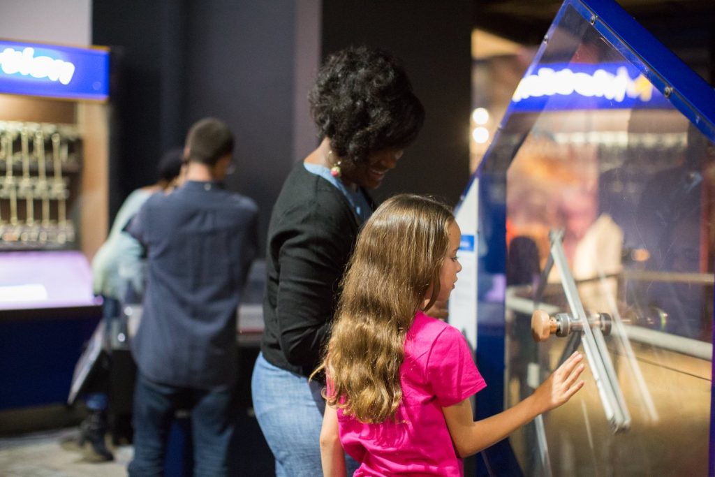 An autistic girl at the Fleet Science Center looking at an exhibit with a caretaker 