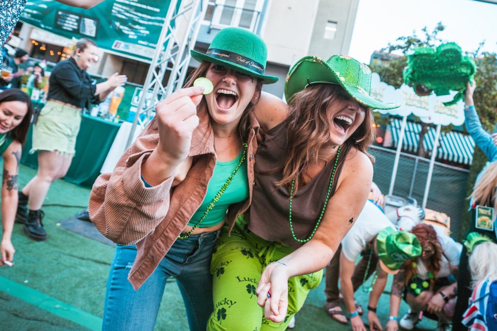 Two women wearing green and holding a gold coin while at the 28th Annual ShamROCK event in the Gaslamp Quarter on March 16