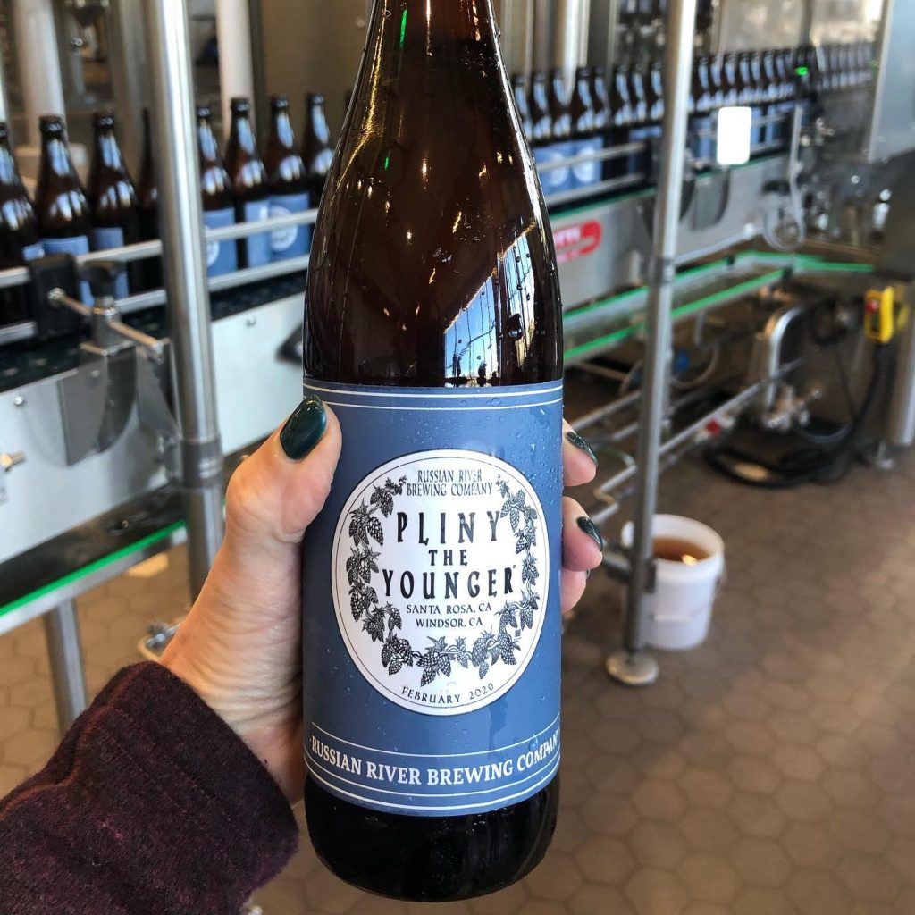 Guerneville's Russian River Brewing company's limited edition Pliny the Younger Triple IPA beer in someone's hand featuring a blue and white label
