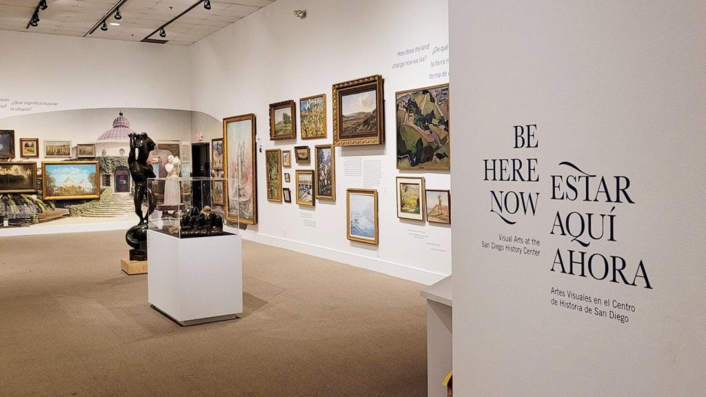 Interior of the San Diego History Center featuring an exhibit called "Be Here Now" with a sculpture and various art on the walls
