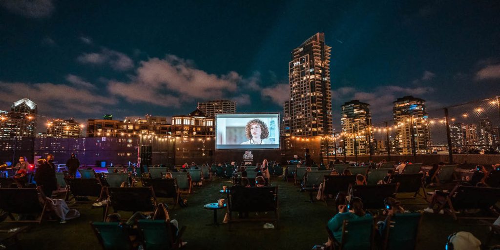 Popular San Diego date spot, the Rooftop Cinema Club located Downtown featuring a movie on a projector on an outdoor patio with people sitting nearby