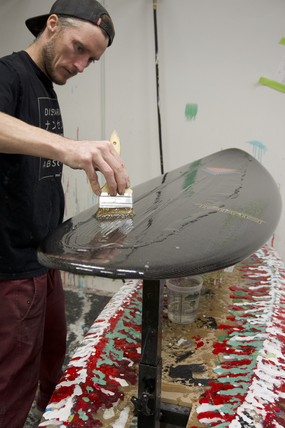 A Dark Arts surfboards employee putting epoxy coating on a carbon fiber surfboard