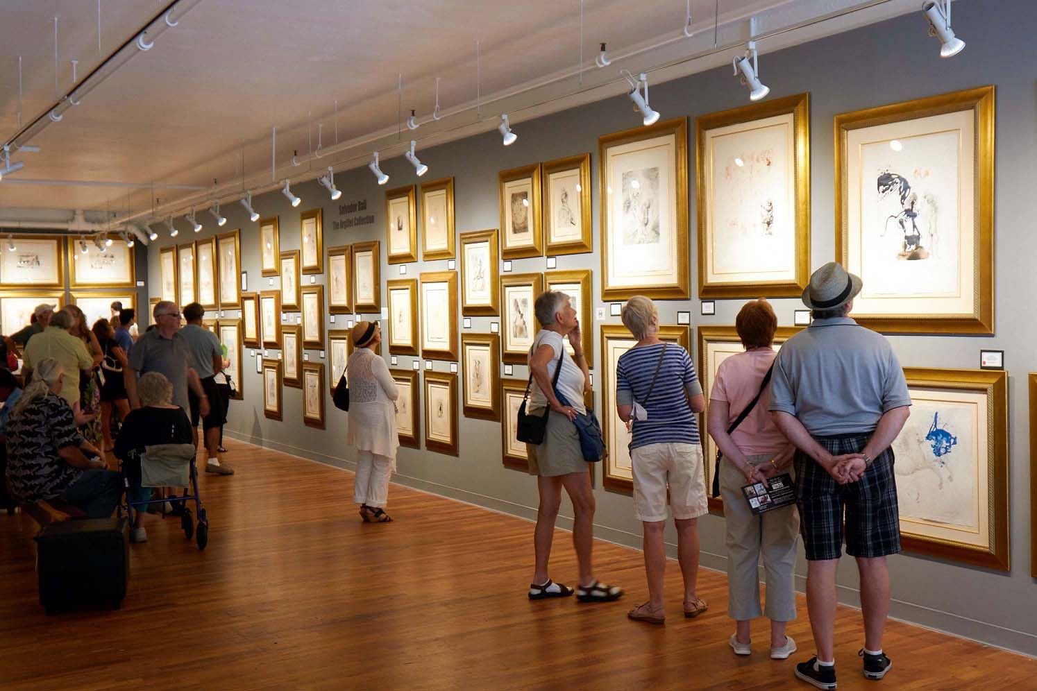 Interior of Meyer Fine Art gallery in Little Italy, San Diego featuring visitors interacting with gold-framed artwork on a wall
