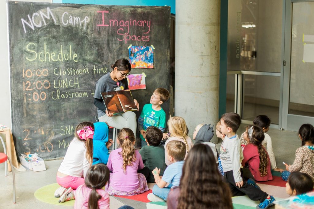Kids reading a book with an instructor during a kids summer camp at The New Children's Museum in downtown San Diego