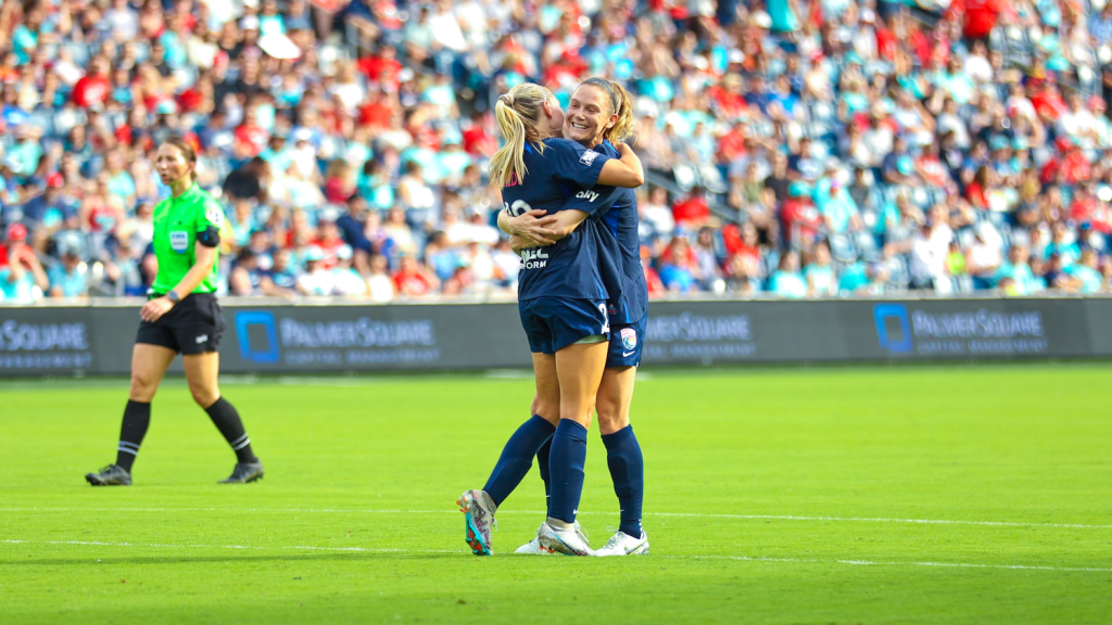 Two San Diego Wave Futbol club players hugging on the field after scoring a goal