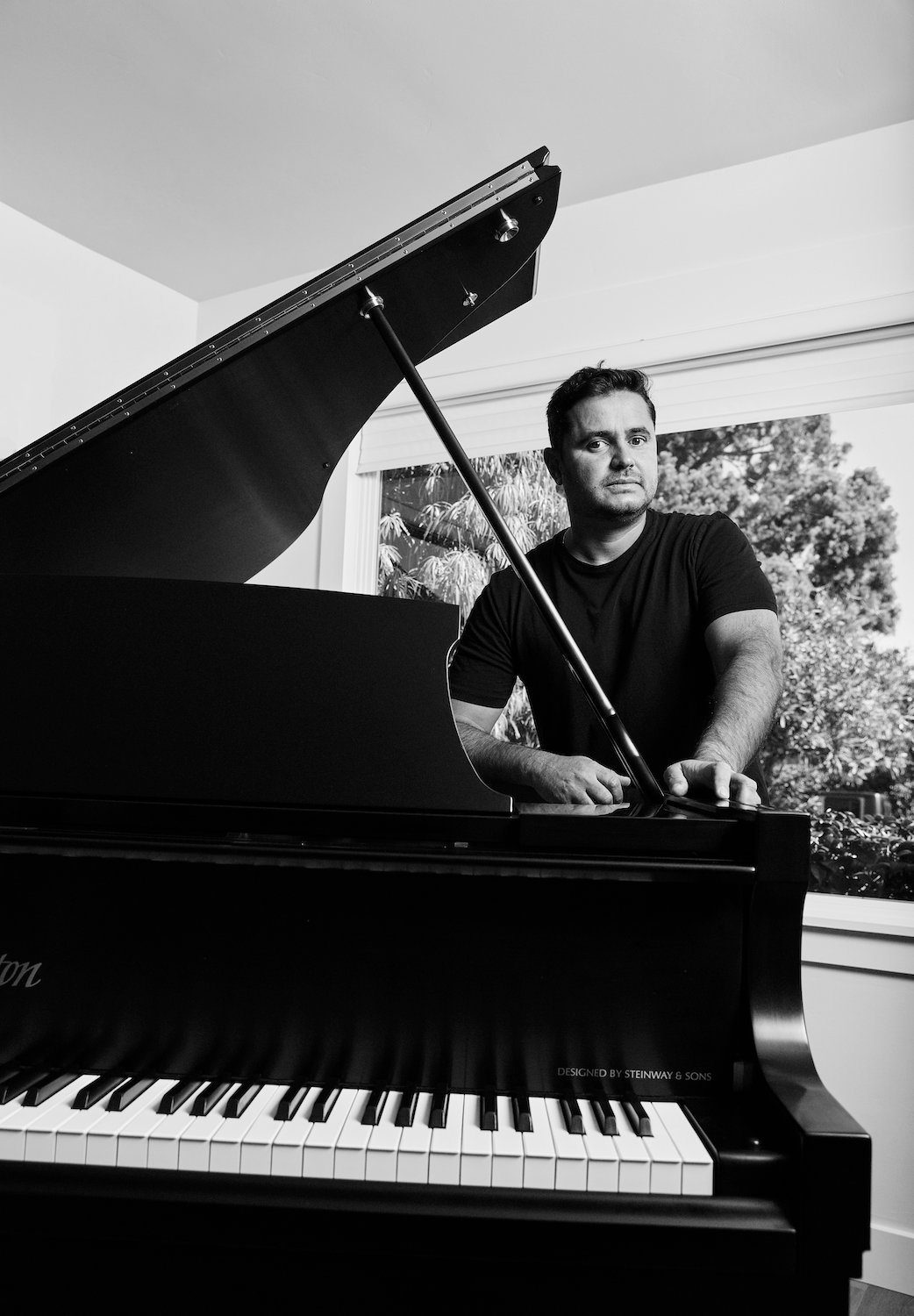 Founder of beverage company Novo Brazil Kombucha, Tiago Carneiro, standing by a piano in black and white