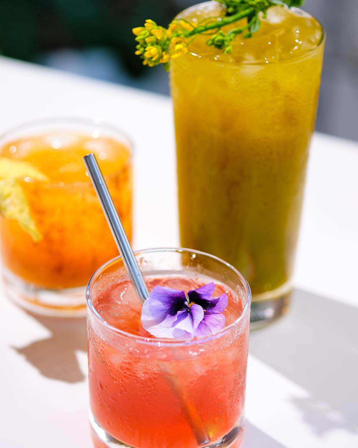 Three icy non-alcoholic mocktail drinks featuring a flower garnish
