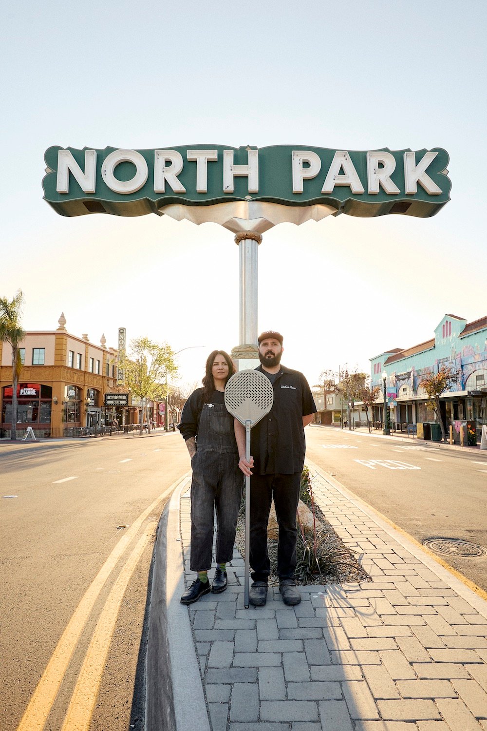 Founders of San Diego restaurant Tribute Pizza standing infront of the North Park sign