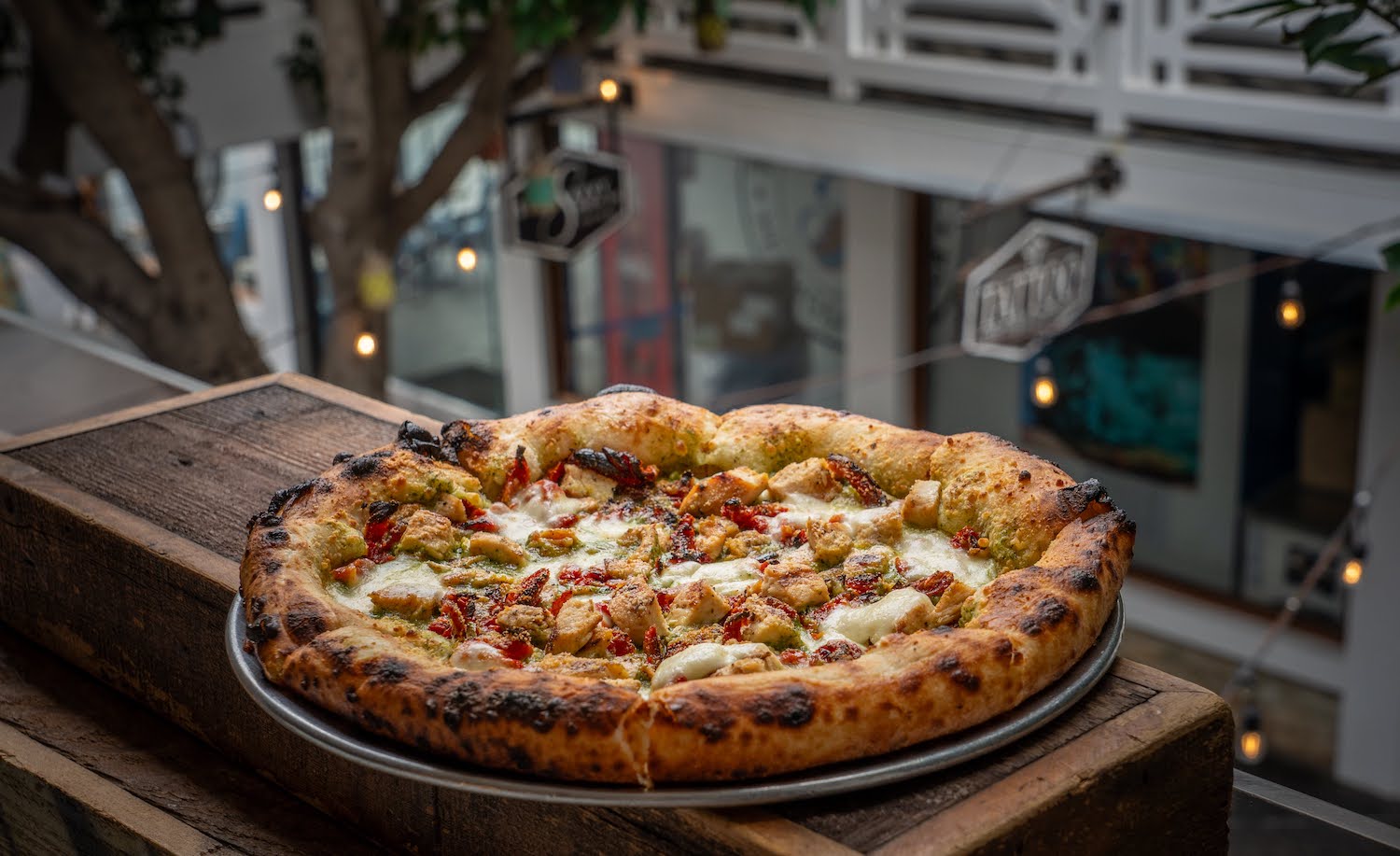 Outdoor patio at new San Diego restaurant and bar Hideaway Pacific Beach featuring a chicken pizza from their wood-fired ovens