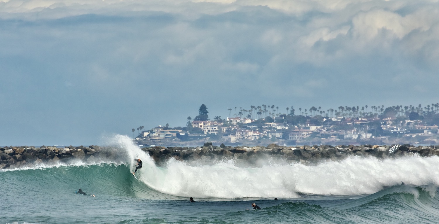 The best surf spots in San Diego featuring Ocean Beach Pier and Jetty with a surfers performing a snap maneuver 
